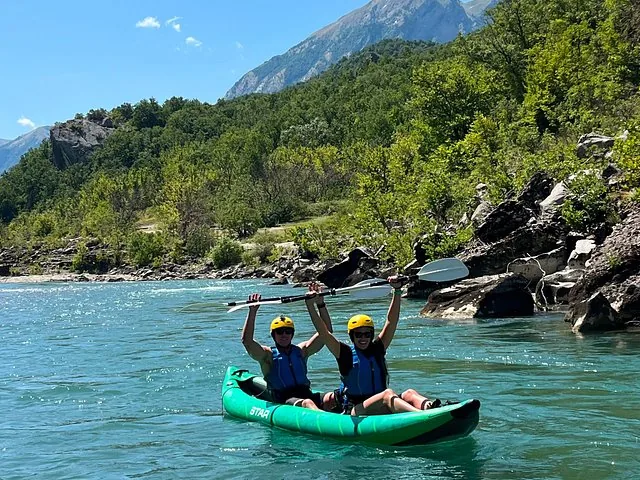 Two people in a green inflatable kayak raising their paddles on a river.