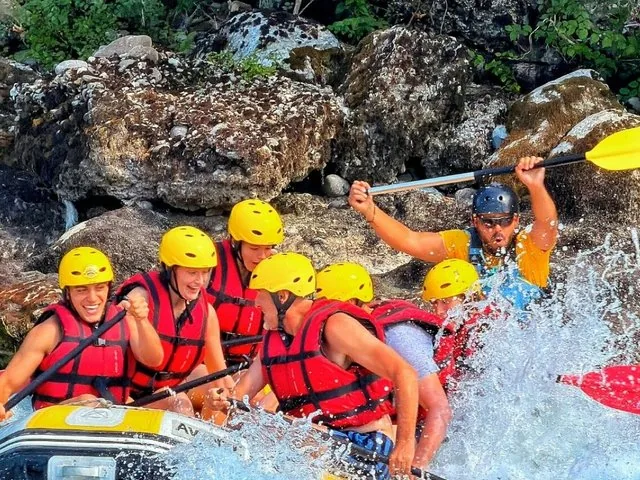 Gruppo di persone con caschi gialli che fa rafting in acque bianche su un fiume roccioso.