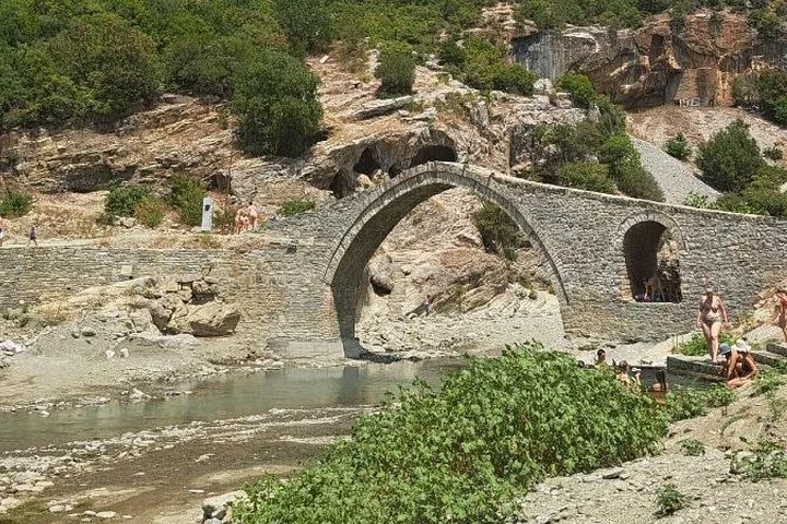 An old stone arch bridge over a river with people relaxing nearby.