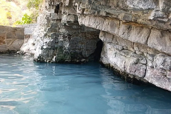 Piccola pozza d'acqua blu alla base di una formazione rocciosa stratificata.